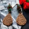Brincos verdes e cor de cobre pousados num tecido de riscas brancas e pretas junto a rosas vermelhas