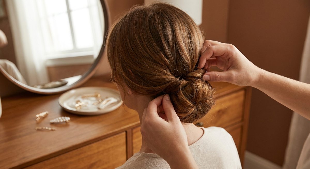 Réalisation d'un chignon bas flou devant un miroir avec accessoires dorés