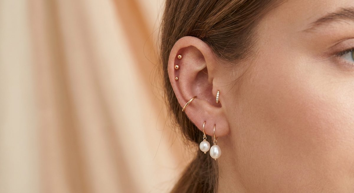 Oreille de femme avec plusieurs piercings : clous dorés sur l'helix, petit anneau au tragus et boucles au lobe
