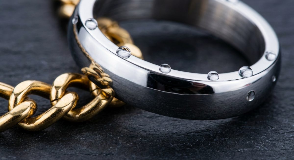 Gros plan d'une bague en acier argenté et d'une chaîne dorée avec des gouttes d'eau