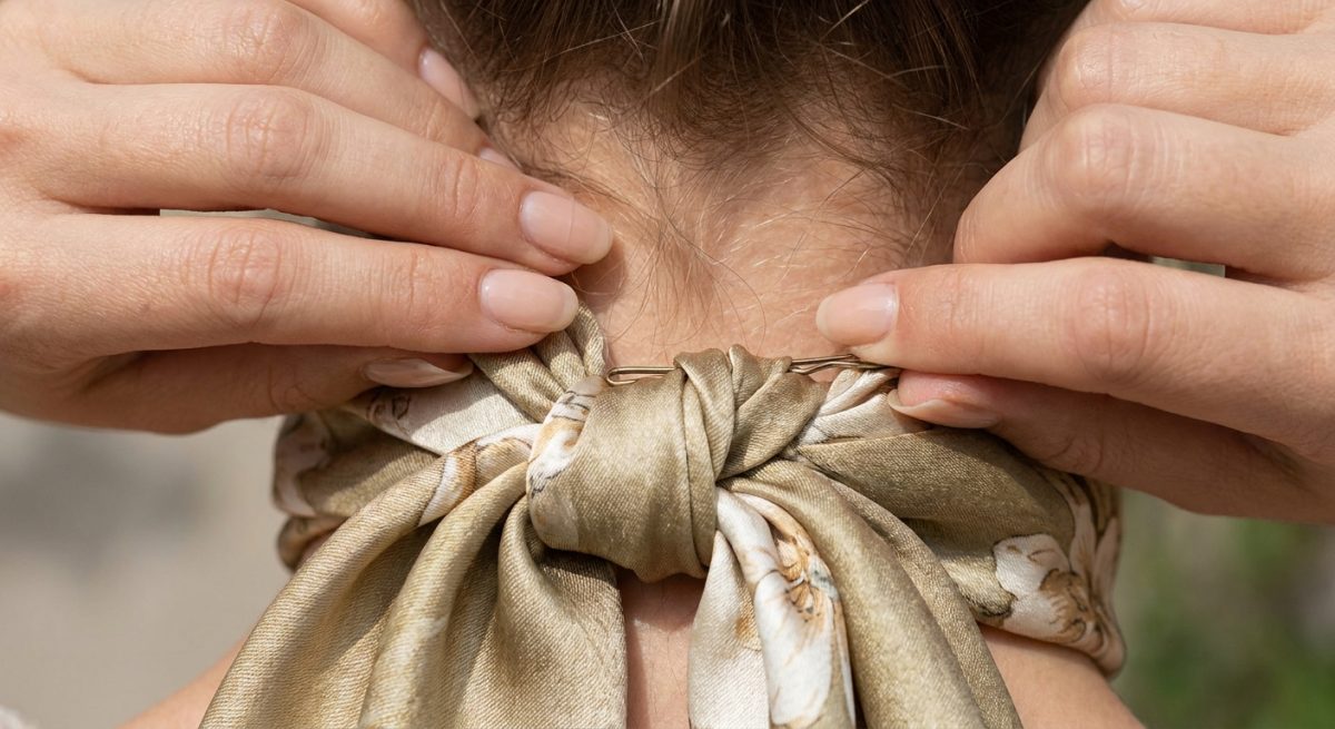 Mains fixant une épingle plate dans le nœud d'un foulard sur la nuque