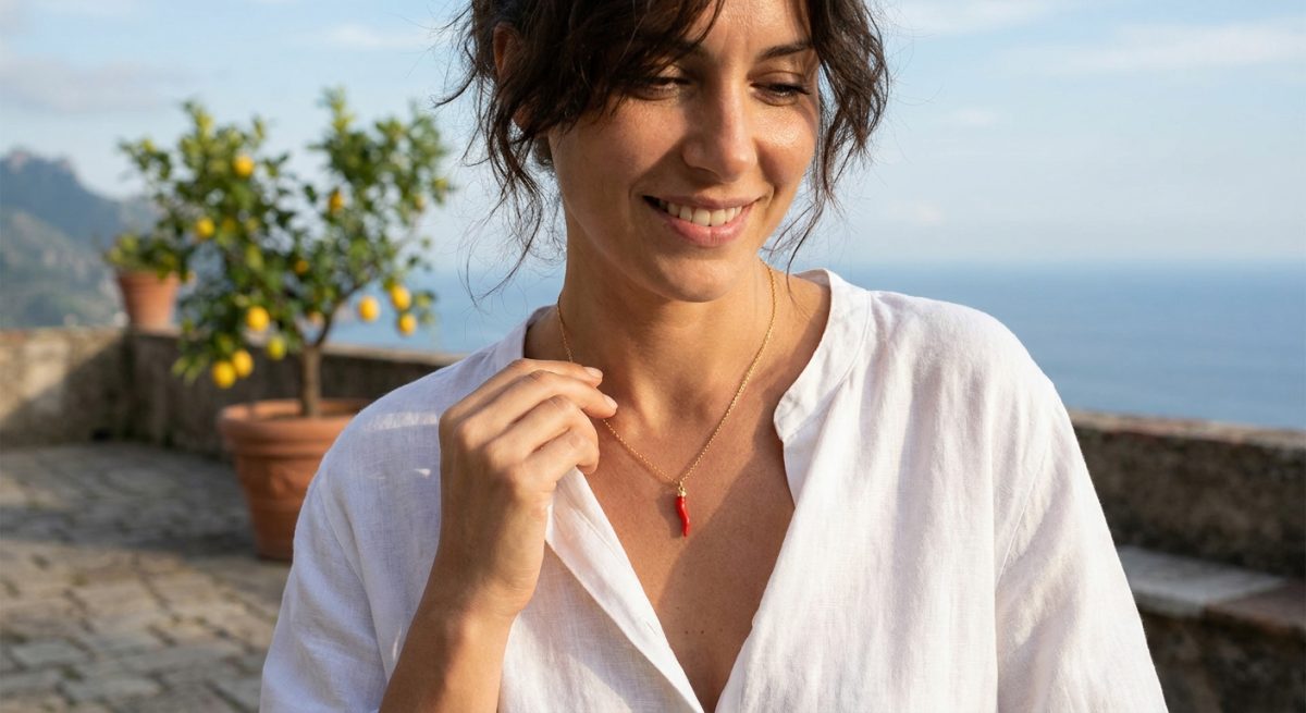Femme portant un collier dore avec petite corne rouge sur chemisier en lin blanc, terrasse italienne