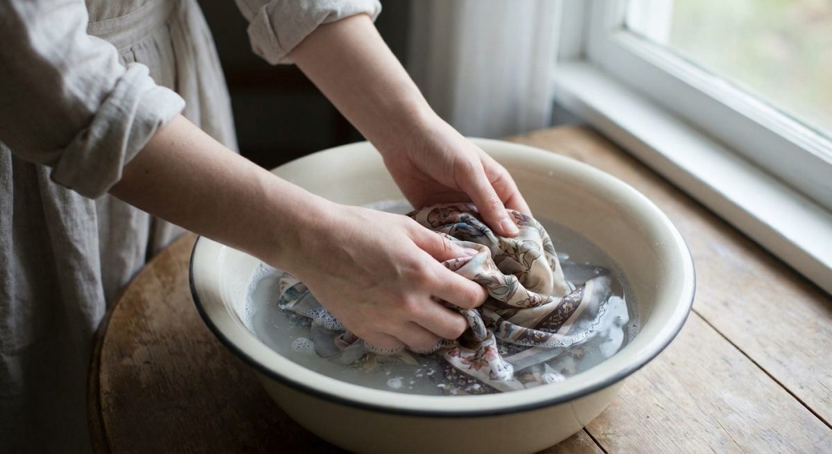 Hands gently hand-washing a colourful silk scarf in a basin of cool soapy water