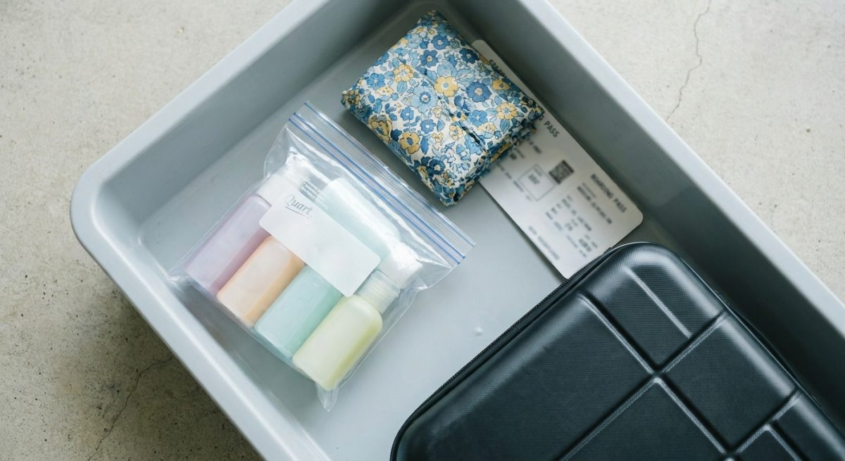 Liquides en bagage cabine : sac transparent, flacons de voyage et pochette en coton sur un bac de contrôle